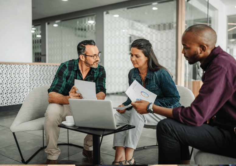 
                  Three consulting professionals in a casual meeting space, reviewing financial documents and a tablet,
                  indicative of the meticulous accounting and bookkeeping services provided for consultants by kept.pro.
                