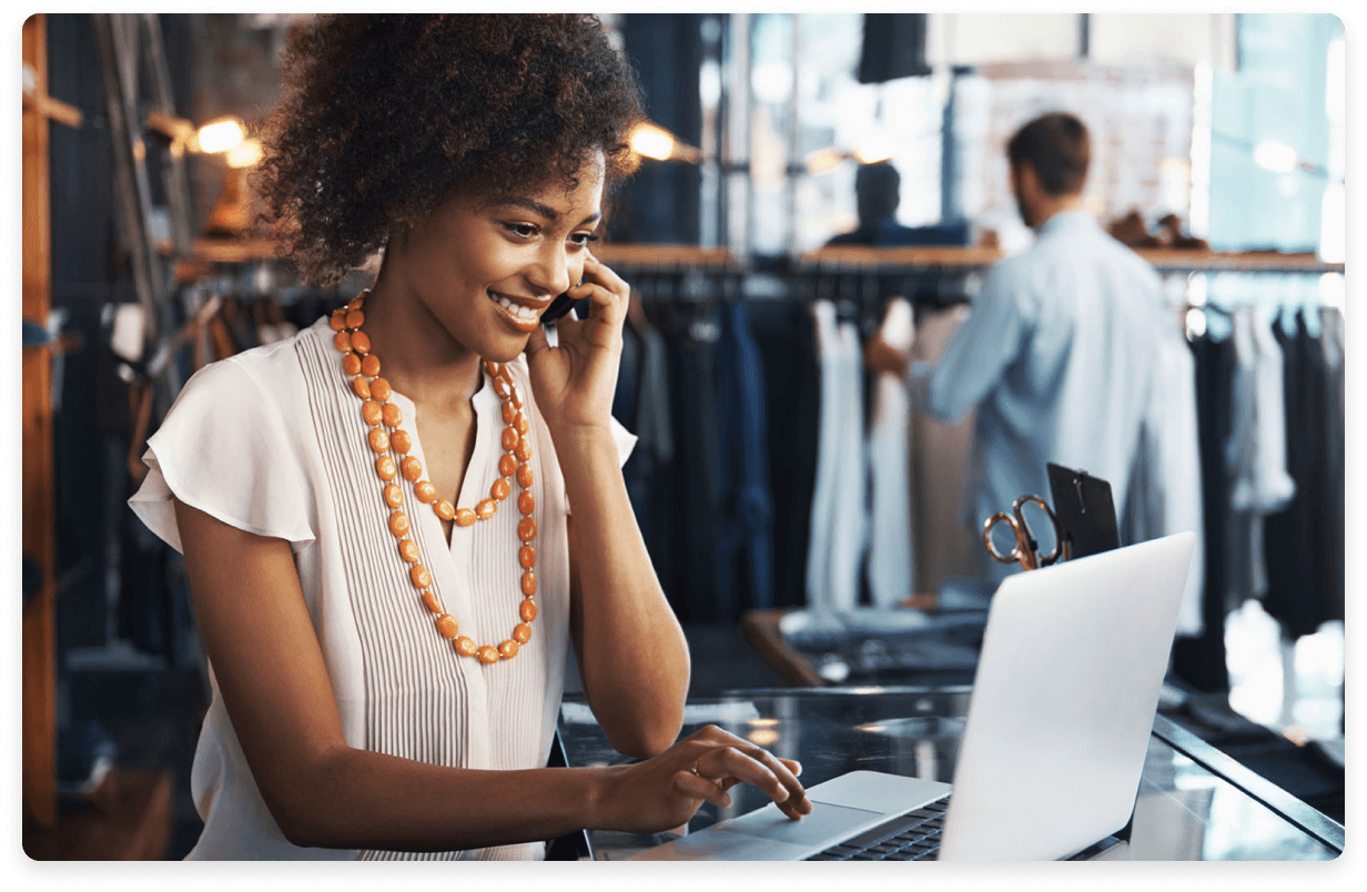 
                  Smiling businesswoman using a laptop and speaking on the phone in a fashion boutique,
                  representing a client-focused approach to financial health and proactive management in a retail setting.
                